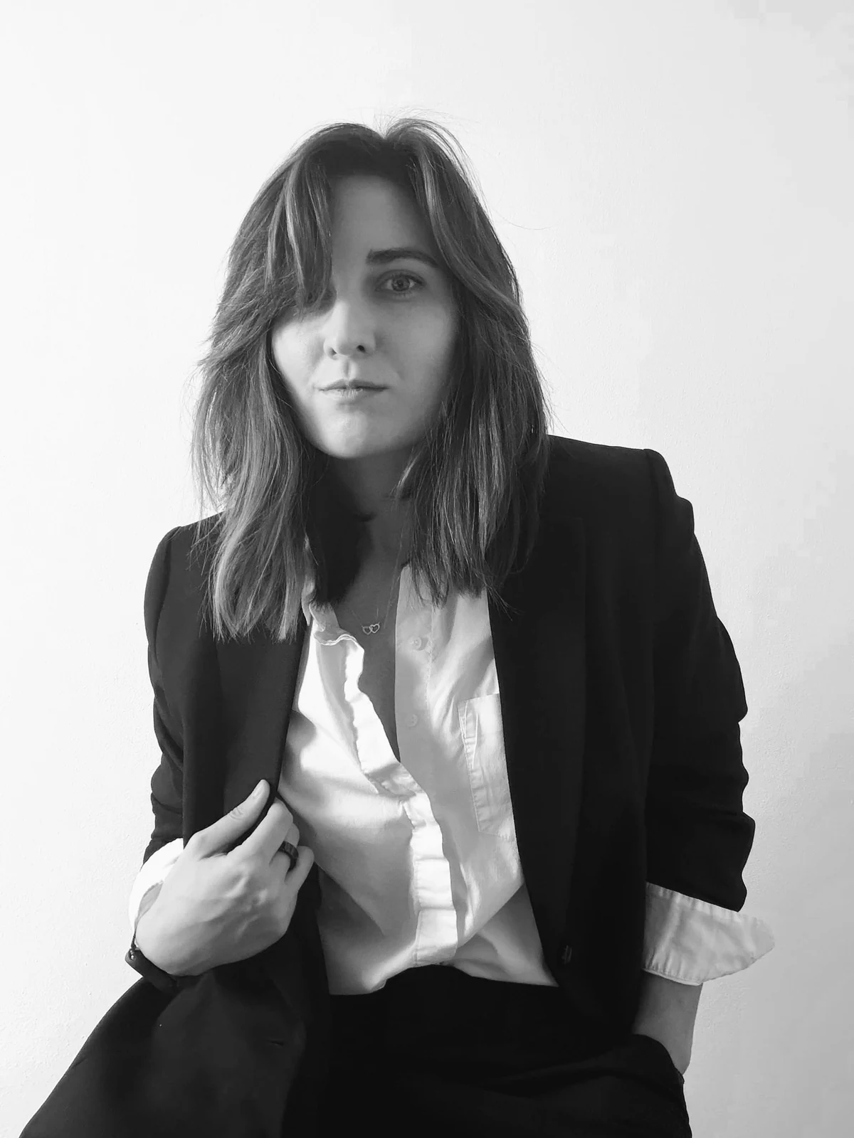 Black and white portrait of Smyxie in a black blazer and white shirt, looking directly at the camera